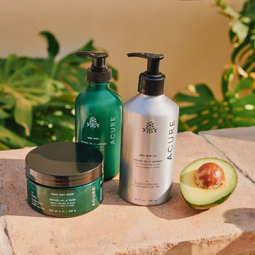 Acure skincare products on a stone surface with an avocado and green leaves in the background